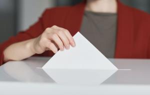 Nahaufnahme einer Hand, die einen Stimmzettel in eine Wahlurne fallen lässt.