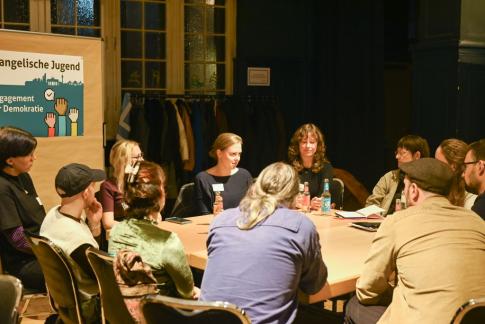 Mehrere Menschen sitzen an einem Tisch und führen eine konzentrierte Diskussion in kleiner Runde.