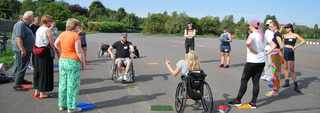 Teilnehmer*innen stehen bei strahlendem Sonnenschein auf dem Tempelhofer Feld und bekommen von den Workshopleiter*innen ein Spiel erklärt.