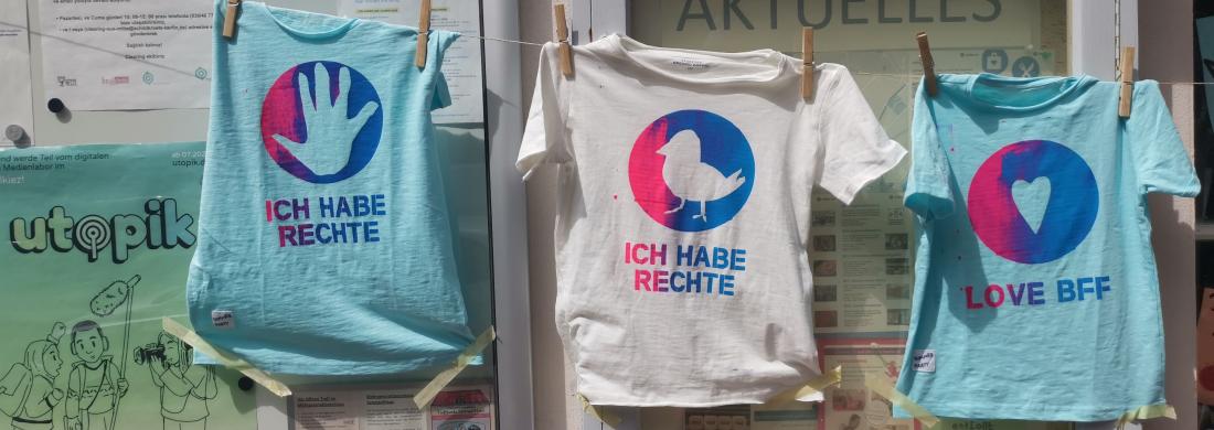 Drei T-Shirts auf einer Wäscheleine, die Kinder mit den Worten "Wir haben Rechte" bedruckt haben