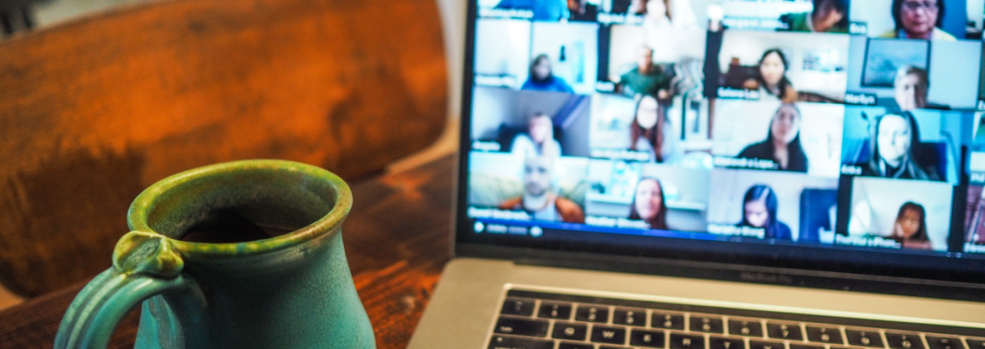 Auf einem Tisch steht ein Laptop auf dessen Bildschirm eine Online-Videokonferenz zu stehen ist, daneben steht eine Tasse