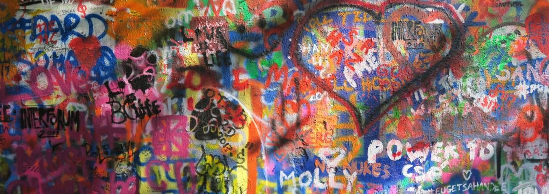 Eine komplett bunte Wand ist in vielen Schichten mit Grafitti, Sprüchen und Namensverewigungen bemalt. Ein großes Herz in der rechten Ecke sticht etwas hervor.