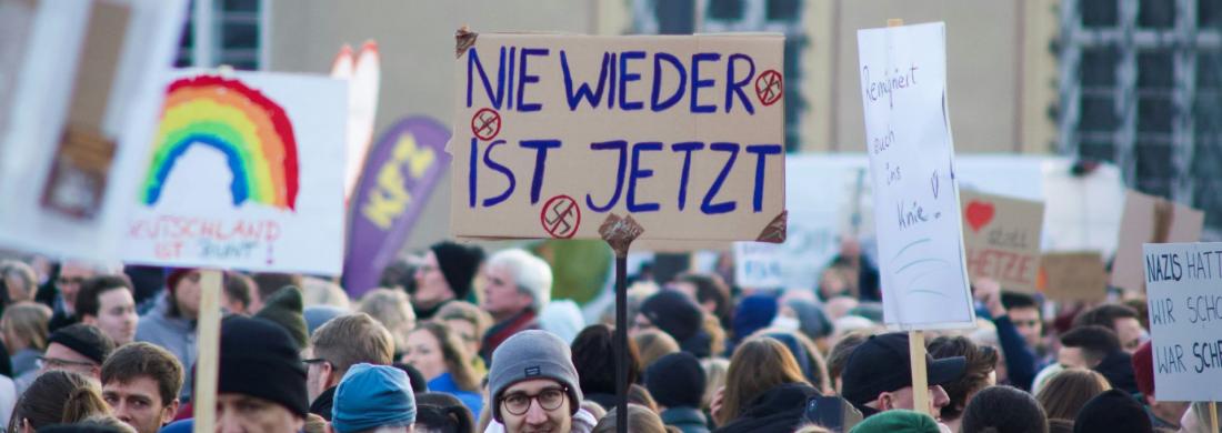 Eine große Gruppe von Menschen bei einer Demonstration. Auf einem Schild in der Mitte steht "Nie wider ist jetzt!"