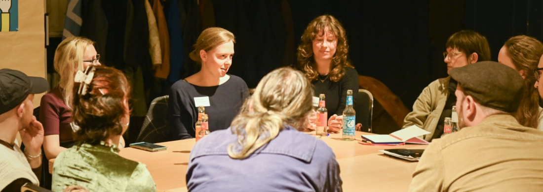 Mehrere Menschen sitzen an einem Tisch und führen eine konzentrierte Diskussion in kleiner Runde.