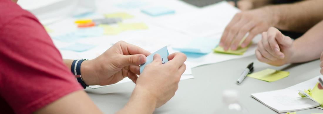Personen sitzen an einem Tisch und halten ihre Ideen auf Papier und Post-its fest.