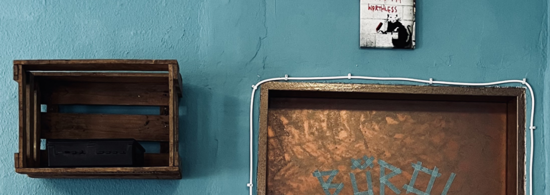 Tür mit Aufschrift "Büro", daneben ein Erste-Hilfe-Kasten, offene Stromleitungen und ein Schild auf dem "Because I'm worthless / Weil ich wertlos bin" steht
