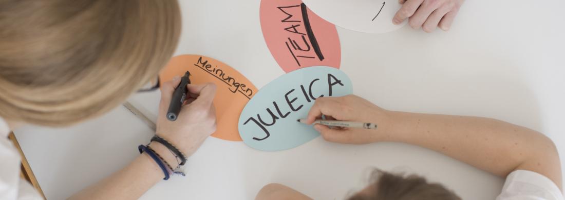 Methoden und Wissen für angehende Jugendleiter:innen und Teamer:innen junge Menschen beschriften Moderationskarten mit Schlagworten wie JuLeiCa, Team und Meinungen