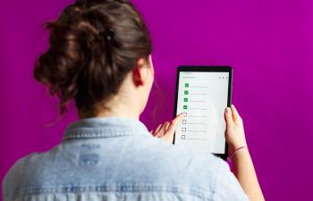 Blick von hinten über die Schulter einer Frau, die ein Tablet mit einer Checkliste in der Hand hält.