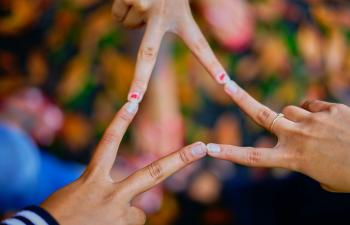 3 Hände strecken Zeige- und Mittelfinger aus, alle Fingerspitzen berühren sich und ergeben ein Dreieck