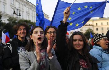 Im Fokus stehen vier Jugendliche bei einer Demonstration mit vielen Menschen im Hintergrund. Die Jugendlichen schwenken die europäische Fahne, eine Jugendliche ruft etwas und klatscht dabei in die Hände.
