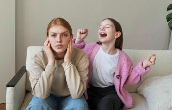 Eine junge Frau hält sich die Ohren zu, während ein junges Mädchen neben ihr laut ist und groß gestikuliert.