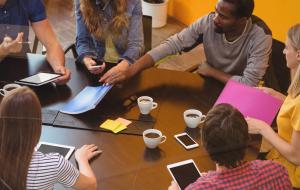 6 unterschiedliche junge Menschen sitzen um einen Besprechungs-Tisch.