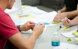 Personen sitzen an einem Tisch und halten ihre Ideen auf Papier und Post-its fest.