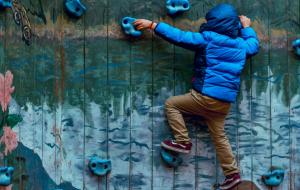 Ein etwa 8-jähriges Kind in einer Daunenjacke klettert an einer Boulderwand nach oben