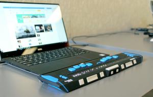 Nahansicht von einem angeschalteten, aufgeklappten Laptop. Vor der Tastatur ist eine Braille-Zeile angebracht.