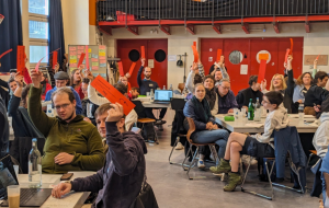 Jugendliche in Versammlung halten rote Karten hoch, aktive Abstimmung, Bühne mit „Jugendliche bewegen Berlin“-Banner.