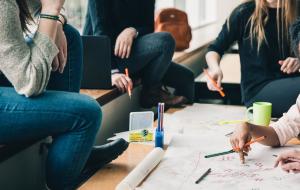 Gruppe junger Menschen arbeitet gemeinsam an einem Tisch mit Skizzen und Markern