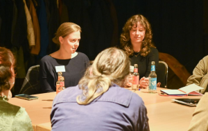Mehrere Menschen sitzen an einem Tisch und führen eine konzentrierte Diskussion in kleiner Runde.