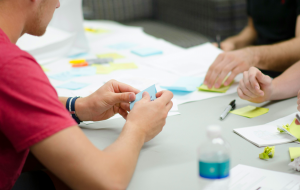 Personen sitzen an einem Tisch und halten ihre Ideen auf Papier und Post-its fest.